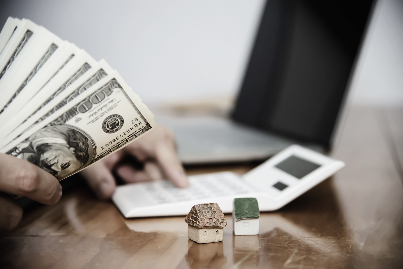 Hand holding cash near calculator and model houses, suggesting business funding or second mortgage planning