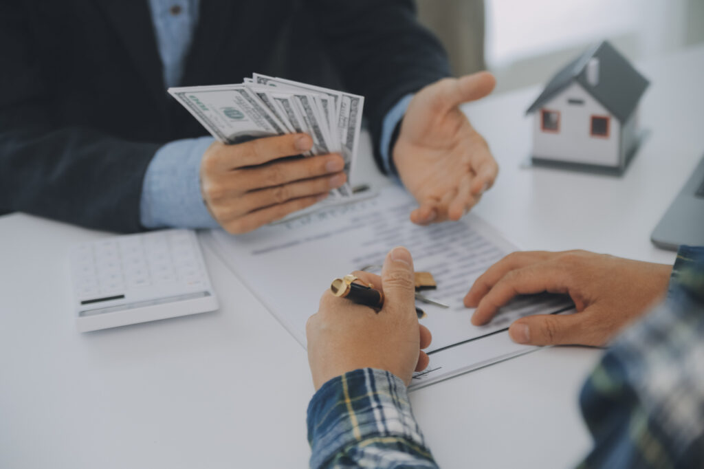 Professional holding cash during a business funding discussion over paperwork, keys and a model house