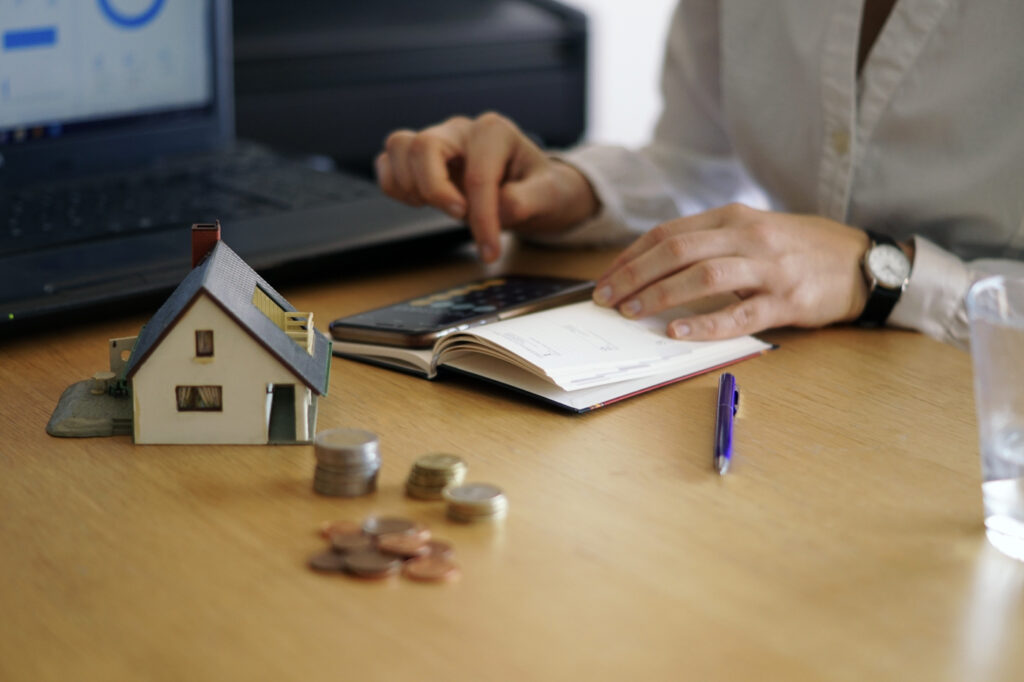 Business owner reviewing notes with calculator beside house model and coins for small business funding